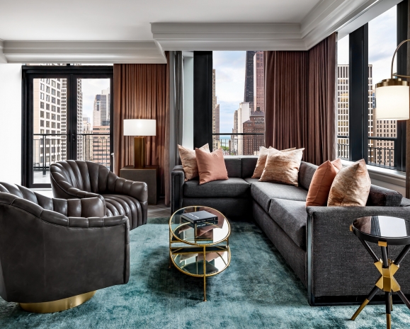 A sectional couch and two leather chairs in a hotel room.