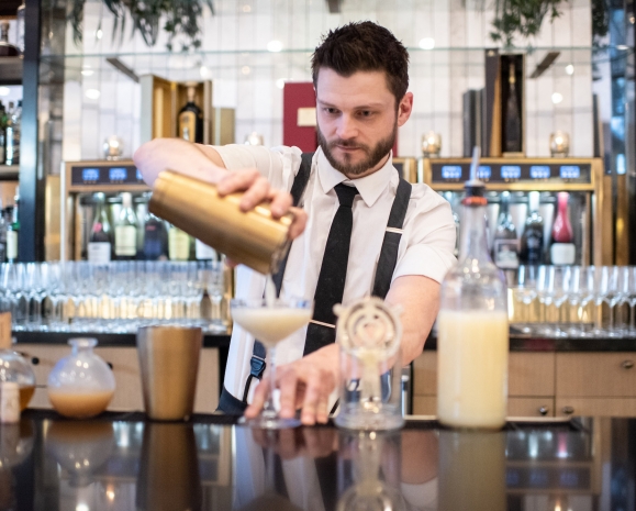 A bartender at Upstairs at The Gwen strains a drink into a cocktail glass.